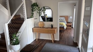 A modern interior with a staircase, a wooden console desk, a mirror, and a bed with a patterned bedspread. - 14 Banksia Parade, Mallacoota (Mallacoota)