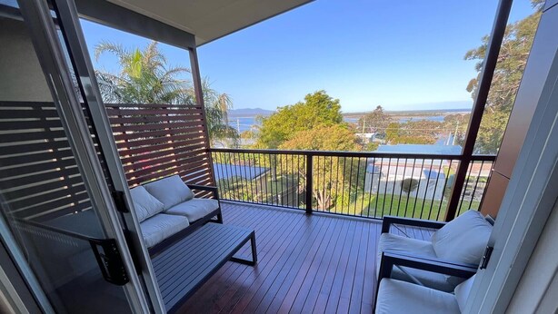 A balcony with a wooden floor, two white cushioned chairs, and a metal railing. - 14 Banksia Parade, Mallacoota (Mallacoota)