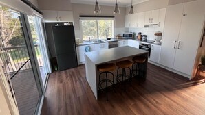 A modern kitchen with a large island, white cabinets, and a sliding glass door leading to a balcony. - 14 Banksia Parade, Mallacoota (Mallacoota)