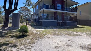 A two-story building with a balcony on the upper floor, a covered outdoor area, and a fenced yard. - 14 Banksia Parade, Mallacoota (Mallacoota)