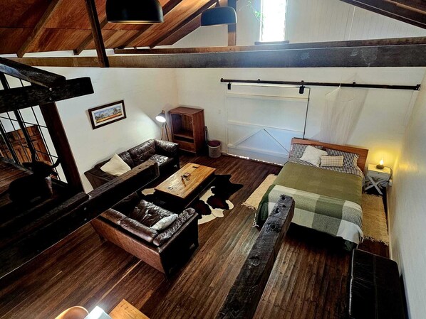 A loft-style room with a wooden ceiling, a sofa set, a bed with a checkered bedspread, a small table, and a lamp. - Barn on the Burnett,
Mundubbera
(Mundubbera)