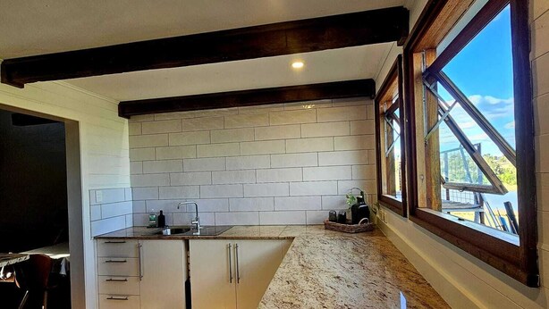 Een moderne keuken met een granieten werkblad, een witte metro betegelde spatwand en houten balken in het plafond.