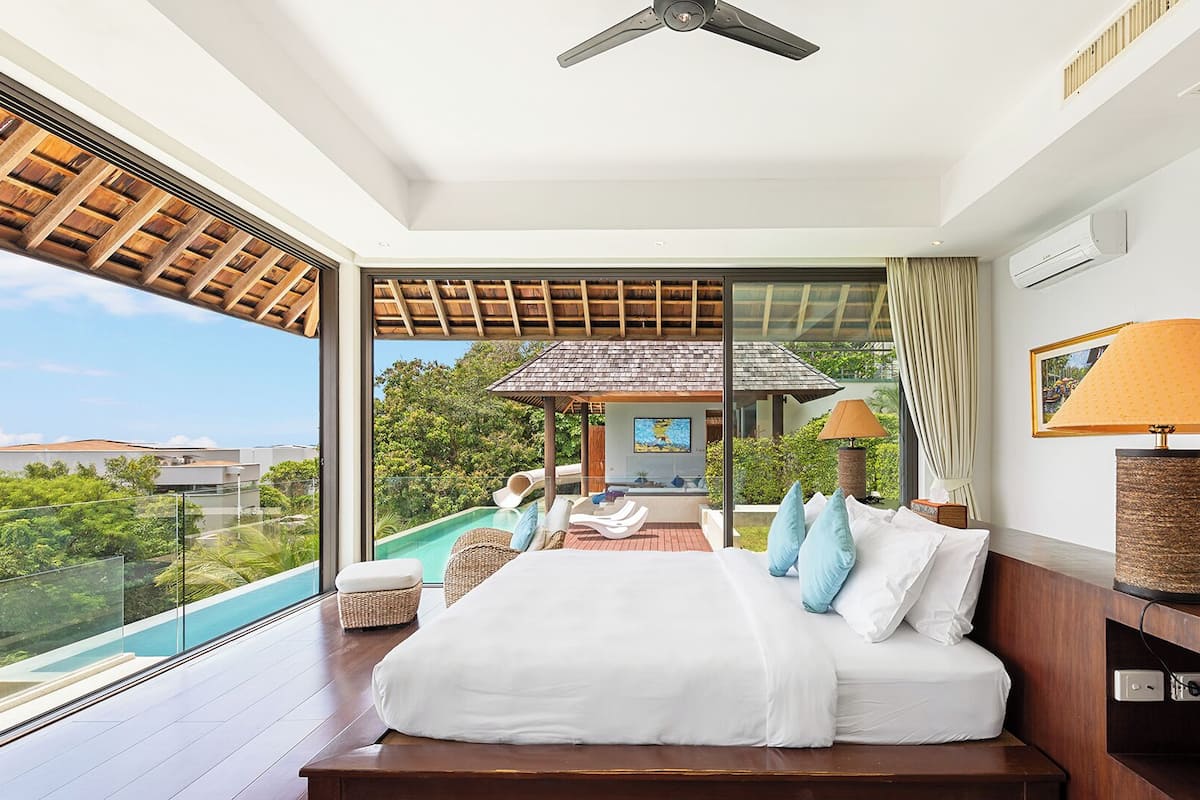 A modern bedroom with a large bed, a view of a pool, and a ceiling fan.