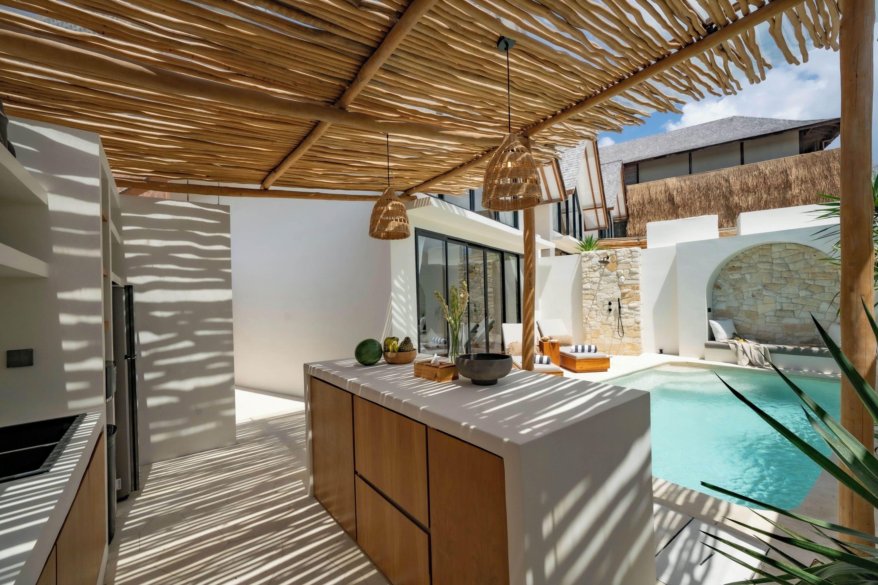 A modern outdoor kitchen area with a pool, wooden cabinets, and a thatched roof.
