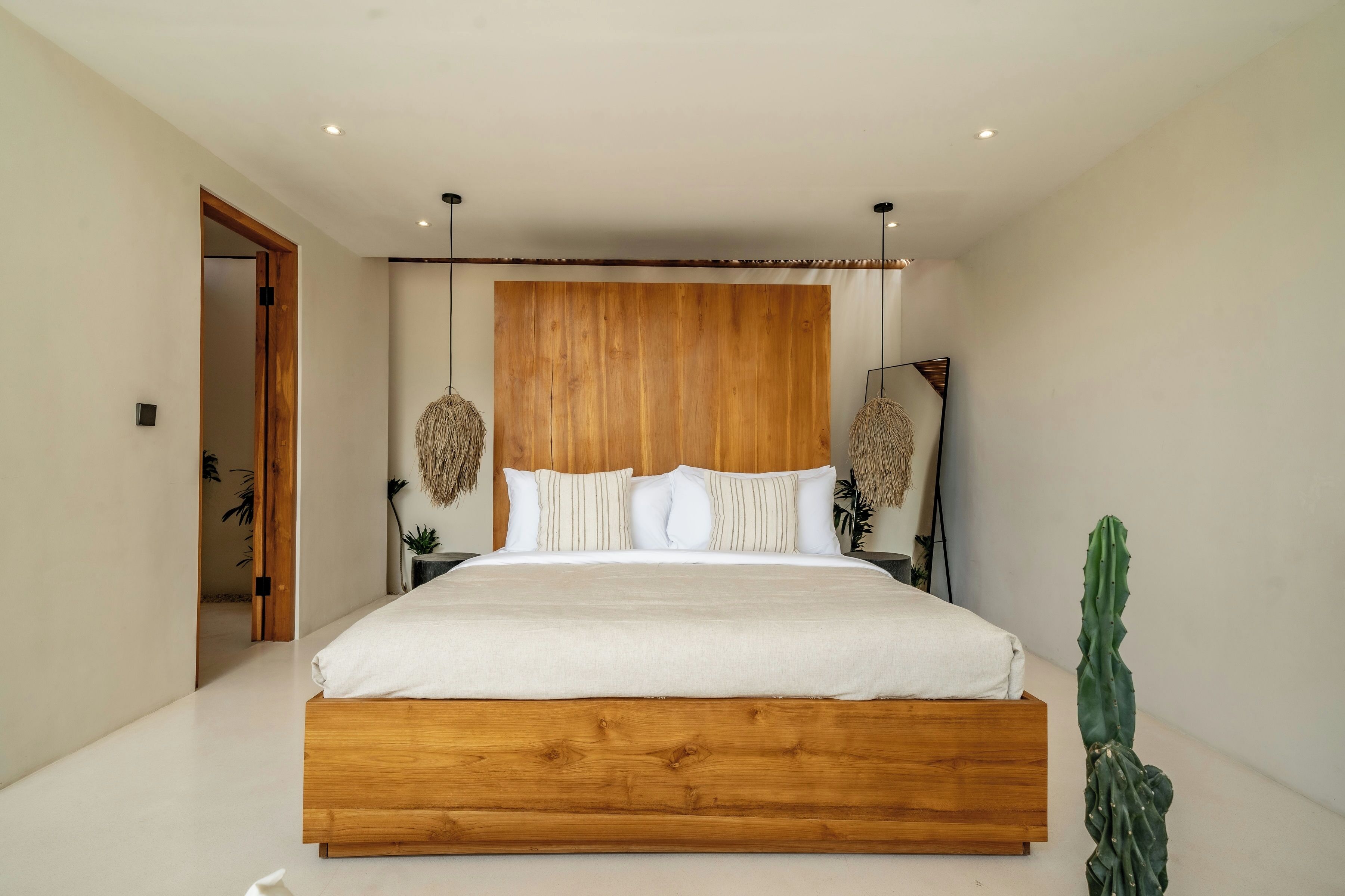 Ein modernes Schlafzimmer mit einem Holzbett, weißer Bettwäsche und einer Kakteenpflanze.