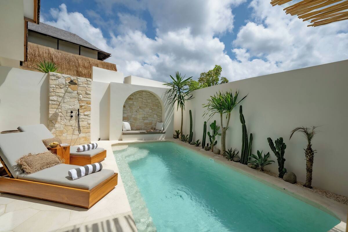 A modern outdoor pool area with a lounge chair, a stone wall, and various plants.