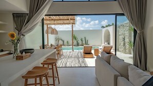 A modern kitchen with a bar area, a dining space, and a view of an outdoor pool area. - 7Seas Bingin (Pecatu)