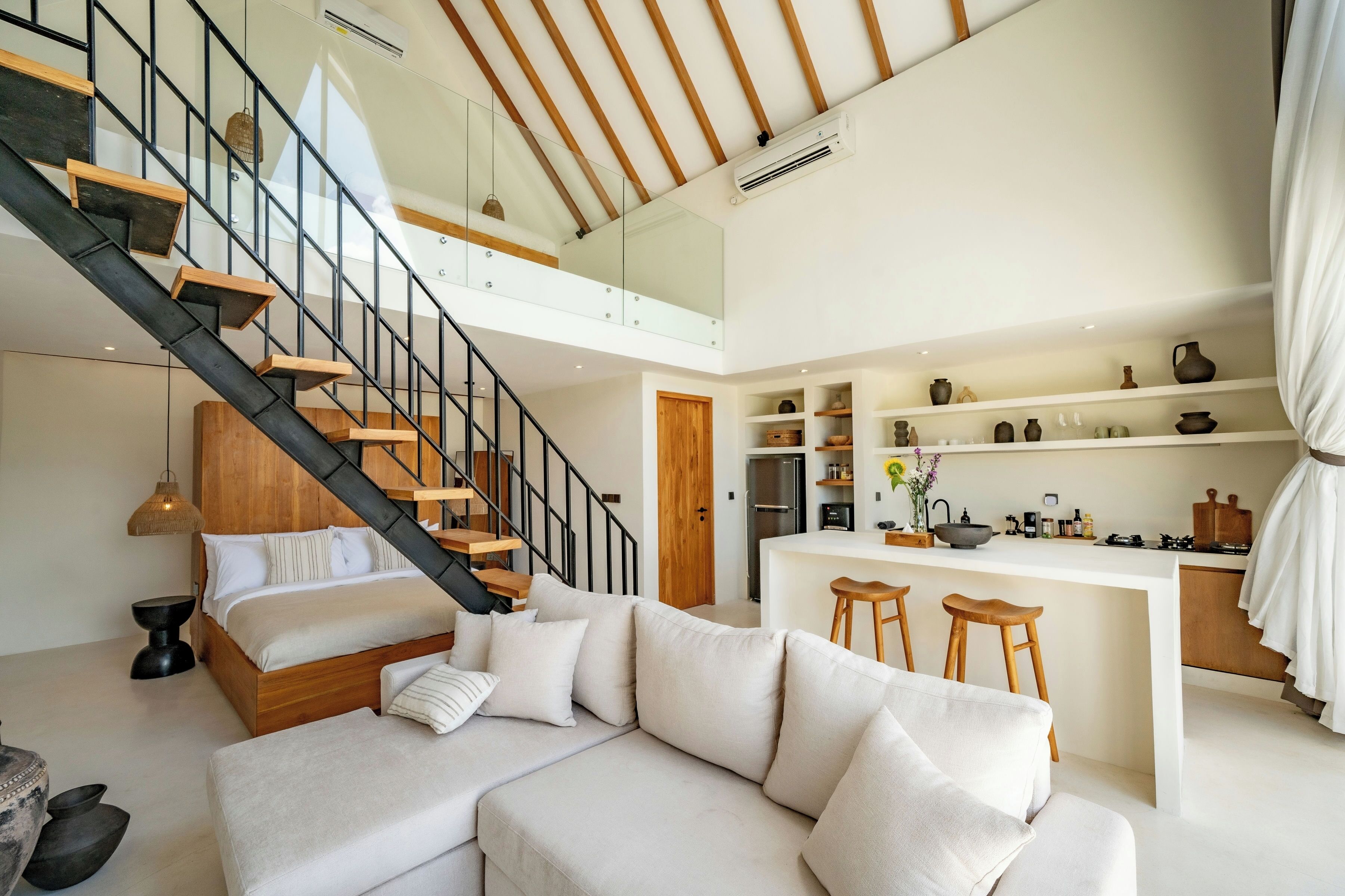A modern interior with a loft bedroom, a kitchen with bar stools, and a dining area.