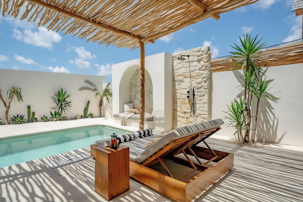 A poolside area with a lounge chair, a wooden table, and a stone wall.