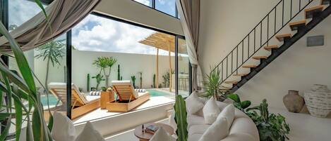 A modern living room with a pool view, a staircase, and a variety of plants.