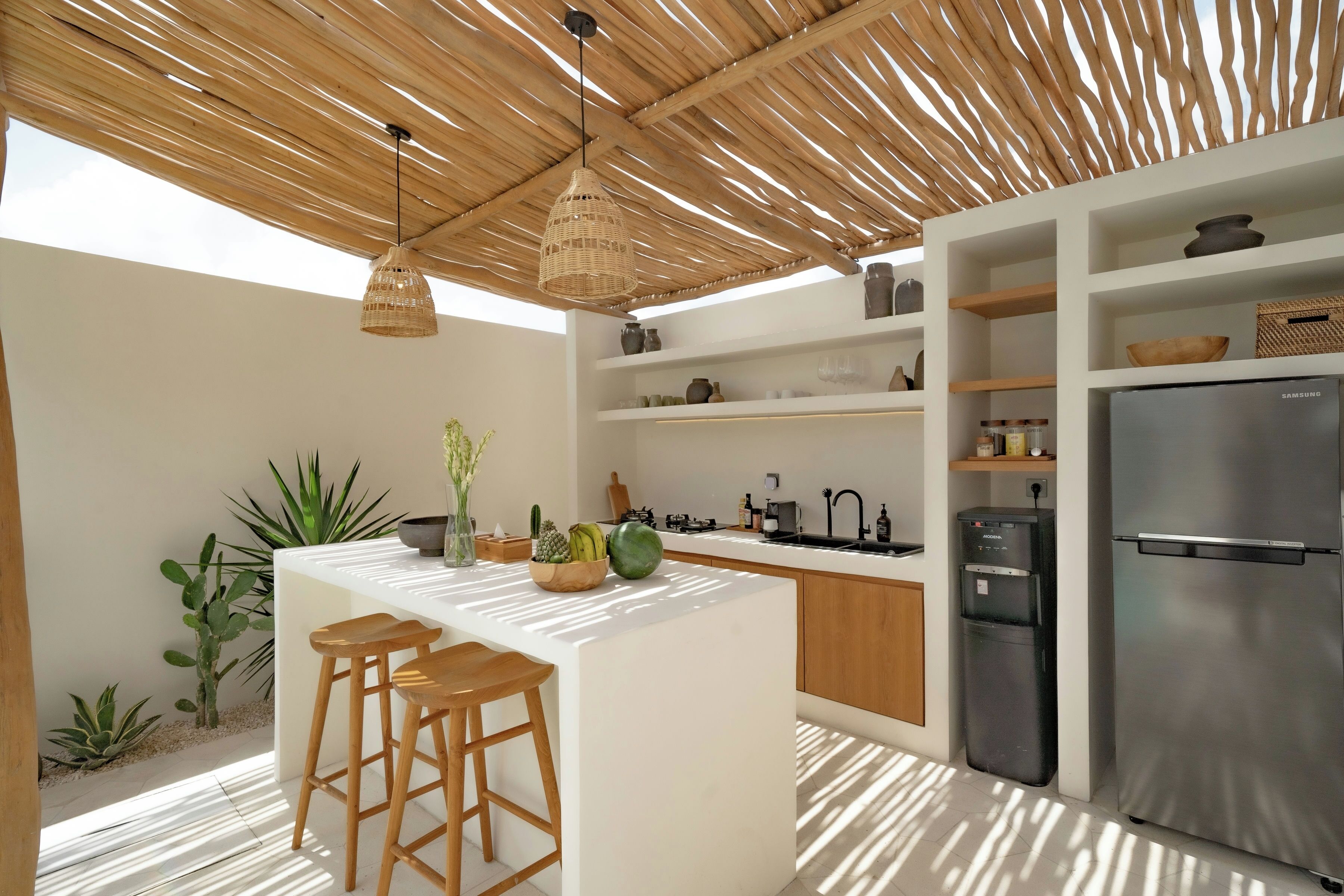 A modern kitchen with a central island, wooden bar stools, a stainless steel refrigerator, and various kitchen appliances.
