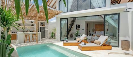 Ein modernes Haus mit Pool, Liegestühlen und einer Bar.
