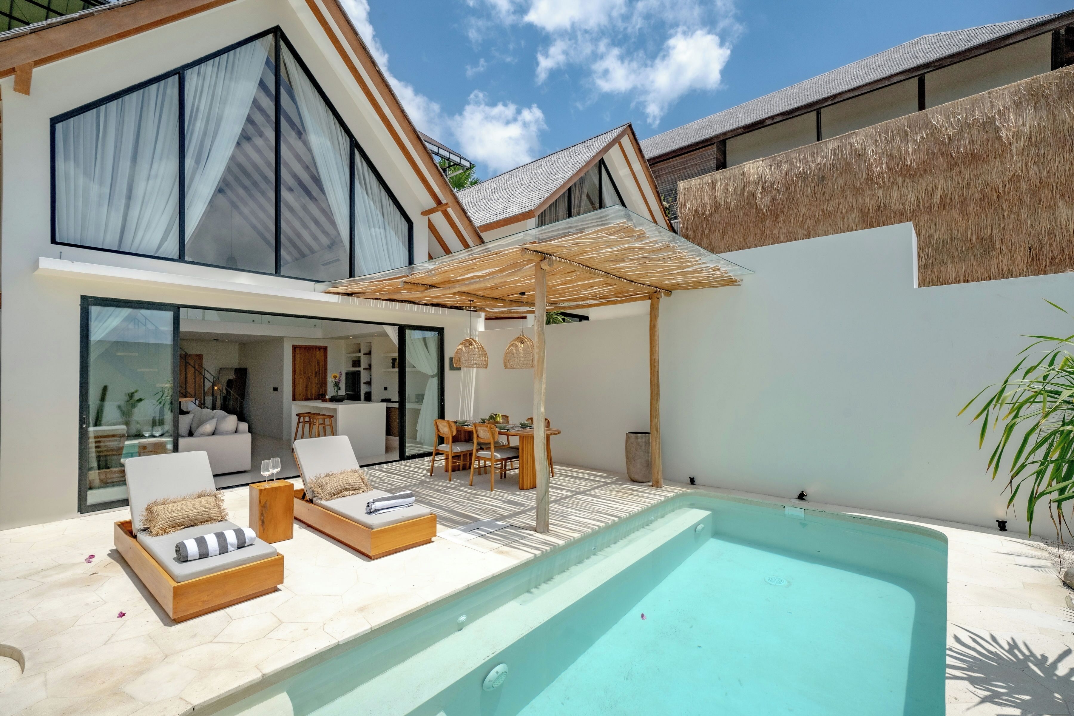 Une maison moderne dotée d’une piscine, d’un coin repas et d’une grande porte vitrée donnant sur un espace de vie.