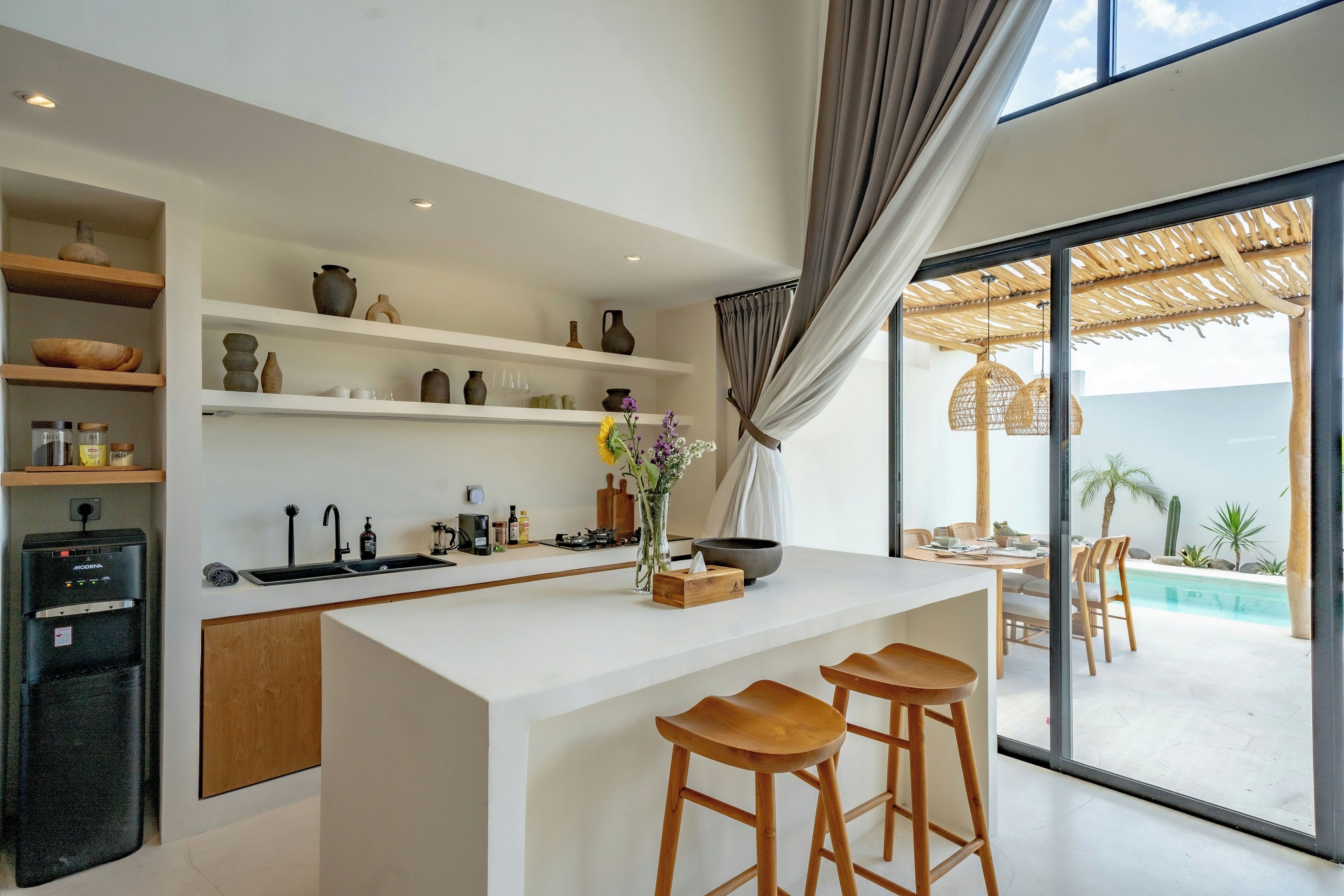 A modern kitchen with white cabinetry, a central island with stools, and a view of an outdoor pool area.