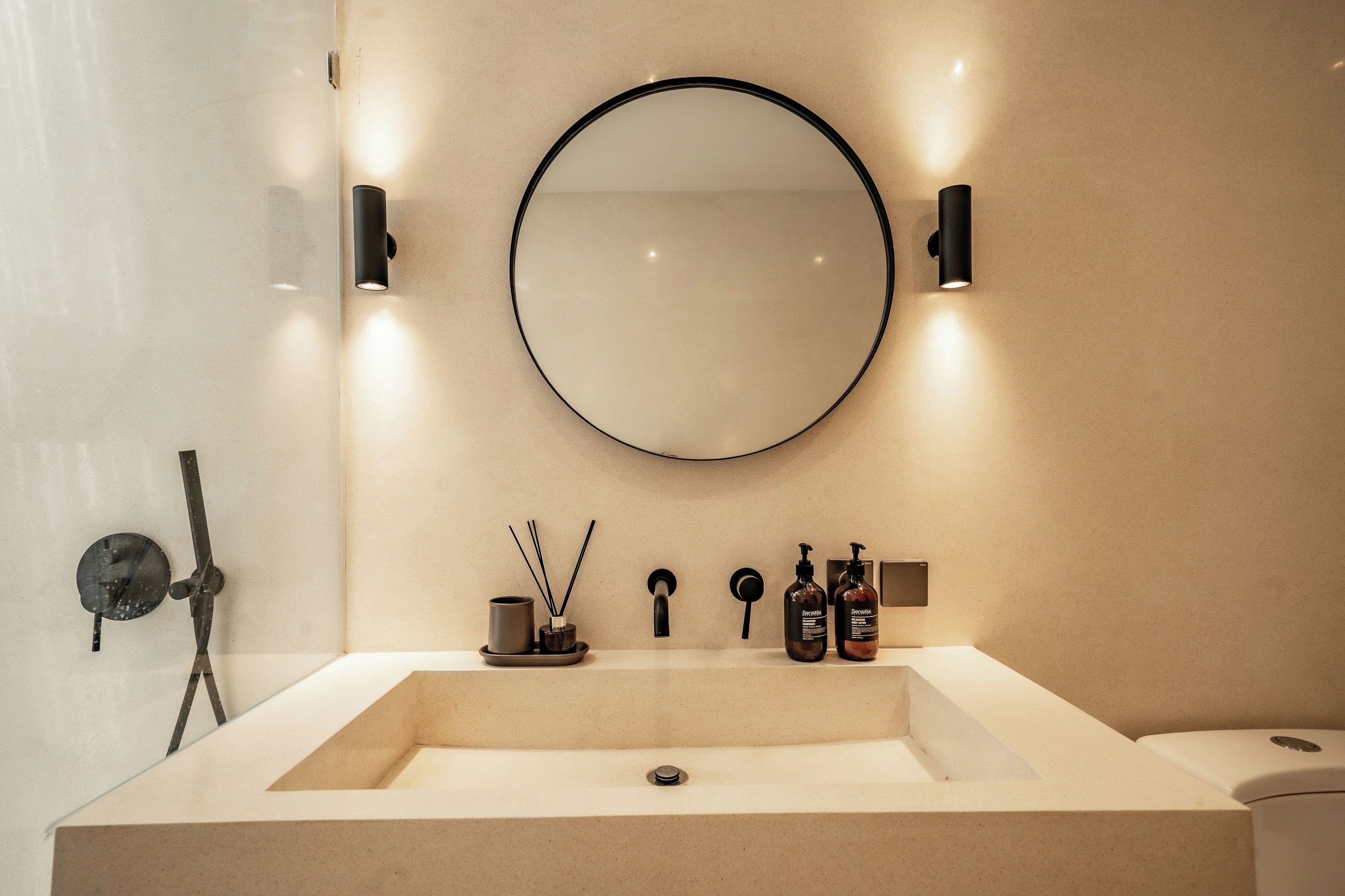 A bathroom with a large rectangular sink, a round mirror, and two wall-mounted lights.