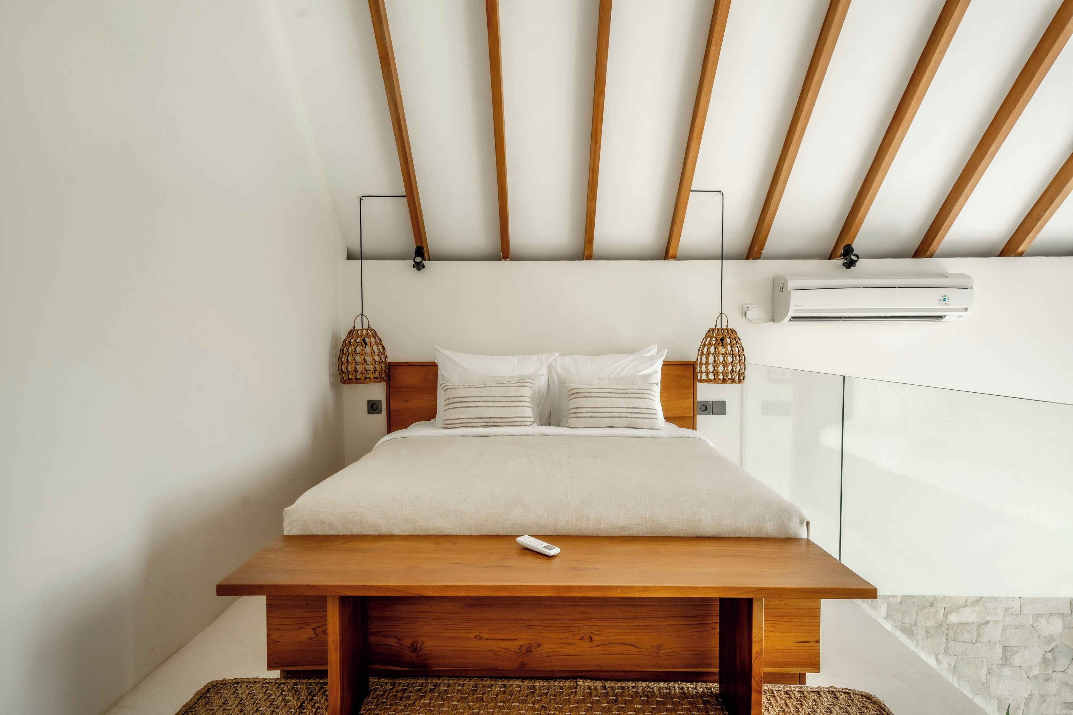 A modern bedroom with a wooden bed frame, white bedding, and a remote control on the nightstand.