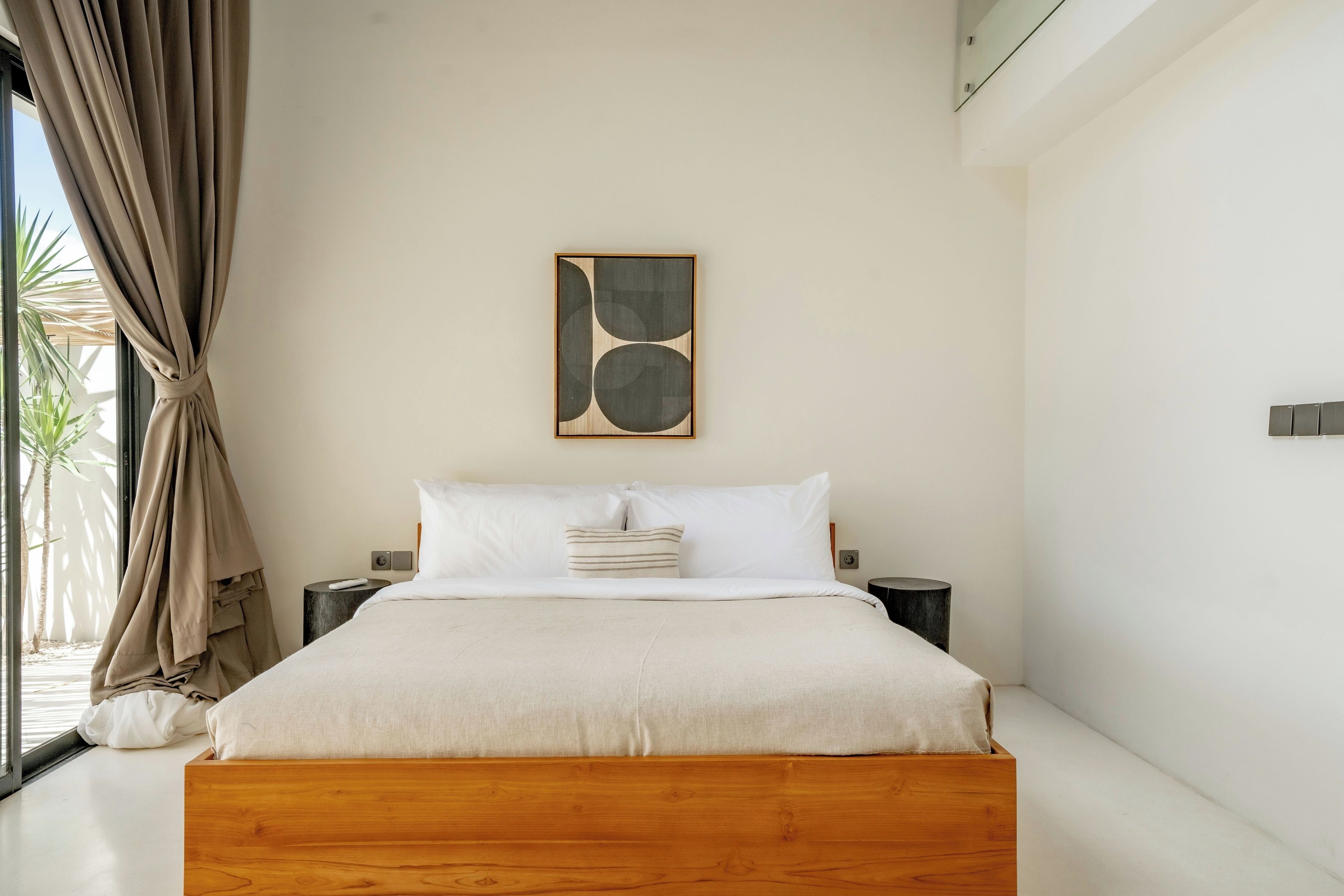 A modern bedroom with a wooden bed, white bedding, and a minimalist abstract painting on the wall.