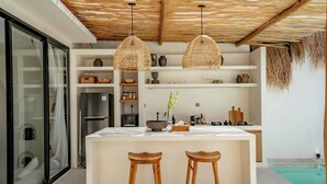 A modern kitchen with a central island, two wooden bar stools, and hanging wicker pendant lights. - 7Seas Bingin (Pecatu)