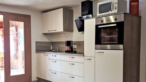 A modern kitchen with white cabinets, a built-in microwave, a coffee maker, and a stainless steel oven.