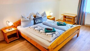A wooden bed with a checkered bedspread and multiple pillows, a bedside lamp, and a small wooden nightstand.
