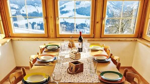 A dining table set for four with a view of snow-covered mountains through large windows.