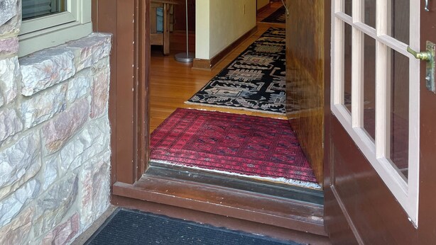 Une porte en bois avec des panneaux de verre, qui donne sur un couloir agrémenté d’un tapis à motifs et d’un mur en pierre.