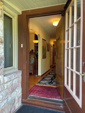 A wooden door with glass panels leading into a hallway with a patterned rug and a stone wall. - Historic 3bd/2ba home in State College-Walk everywhere WiFi “Lucky Rabbit Lodge” (State College)