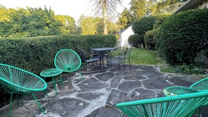 Un espace extérieur aménagé en terrasse, avec un sol en pierre et des chaises et tables en métal vert.