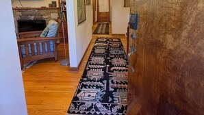 Un couloir avec un plancher en bois, un tapis à motifs, un téléviseur, une lampe et une porte dotée d’une poignée.