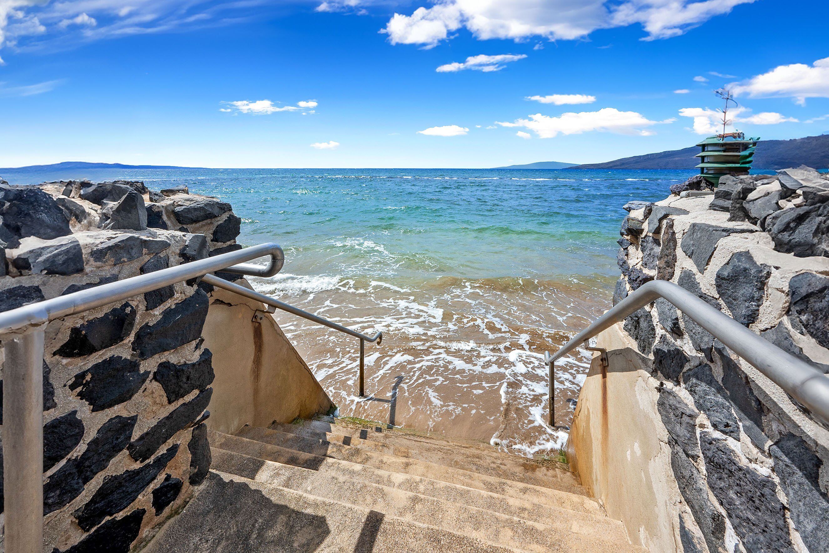 A staircase leading to a rocky shore with a view of the sea and distant mountains.