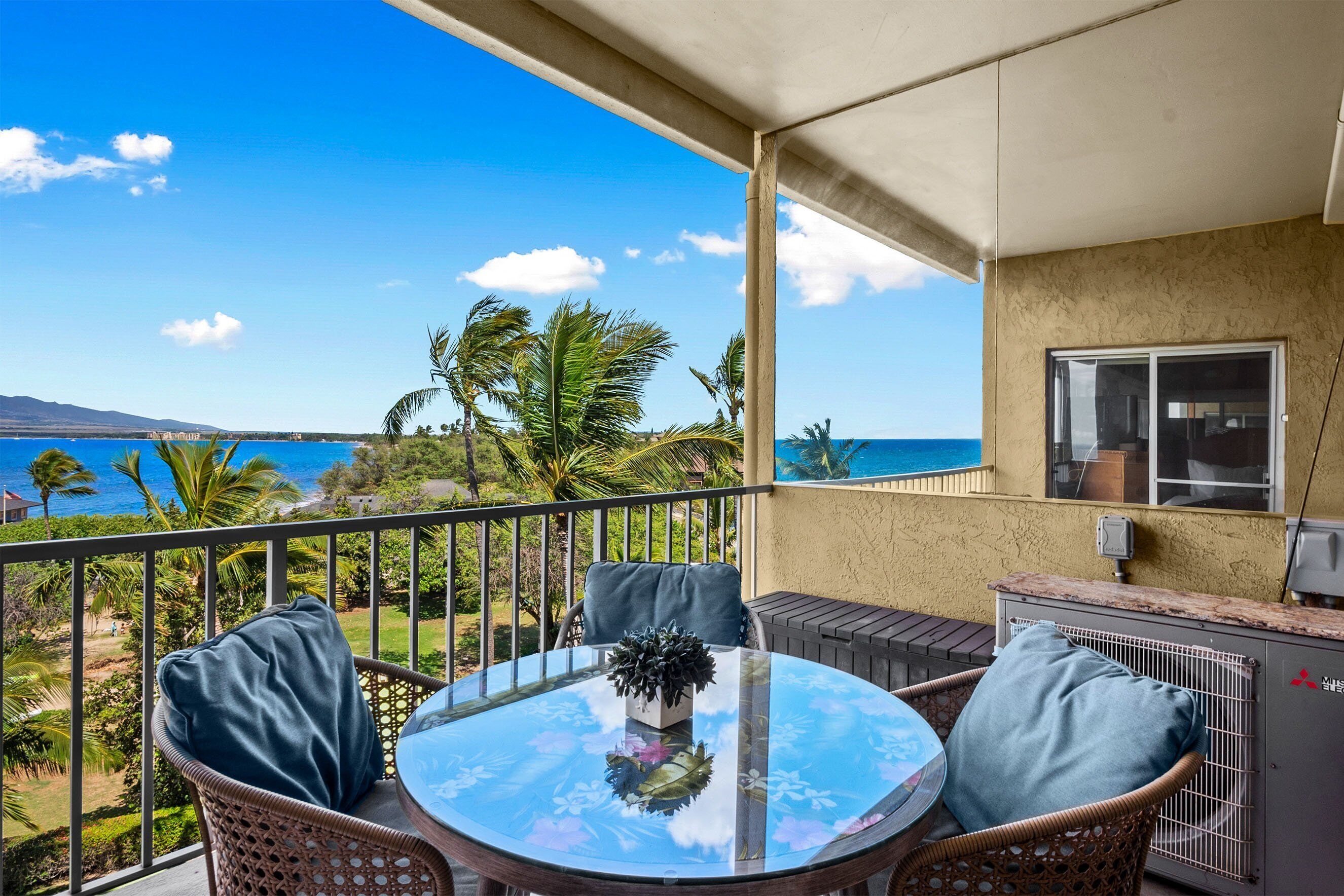 A balcony with a glass table, wicker chairs, and a view of the ocean.