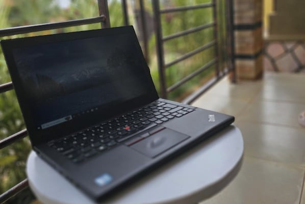 A laptop on a small round table with a view of greenery outside.