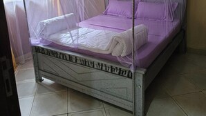 Una cama con mosquitero, almohada blanca y colcha morada.