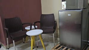 Una kitchenette con microondas y refrigerador, dos sillas de mimbre y una mesita blanca.