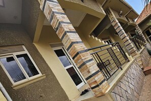 A multi-story residential building with a stone facade, a balcony with a metal railing, and a window with a view of the sky. - Quiet Apartment with Fast Wifi - Kisaasi Kampala (Kampala)
