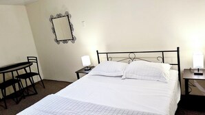 Une chambre d’hôtel comprenant un lit, un bureau avec une chaise, une table de chevet avec une lampe et un miroir fixé au mur.