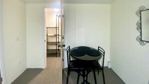 Une petite pièce étroite, avec une table et des chaises, une étagère en métal et un miroir accroché au mur.
