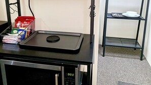 Une petite cuisine équipée d’un four à micro-ondes, d’une machine à café et d’une étagère avec des tasses et une cafetière.