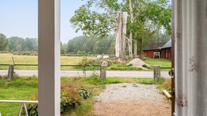 Landelijke omgeving met een onverharde pad dat leidt naar een houten hek, een grote boom en een rood gebouw op de achtergrond.