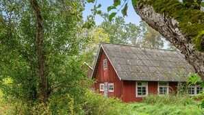 Een rode houten woning, omringd door weelderige begroeiing en bomen.