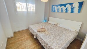 Een slaapkamer met een bed, houten vloer, een raam en een schilderij aan de muur.