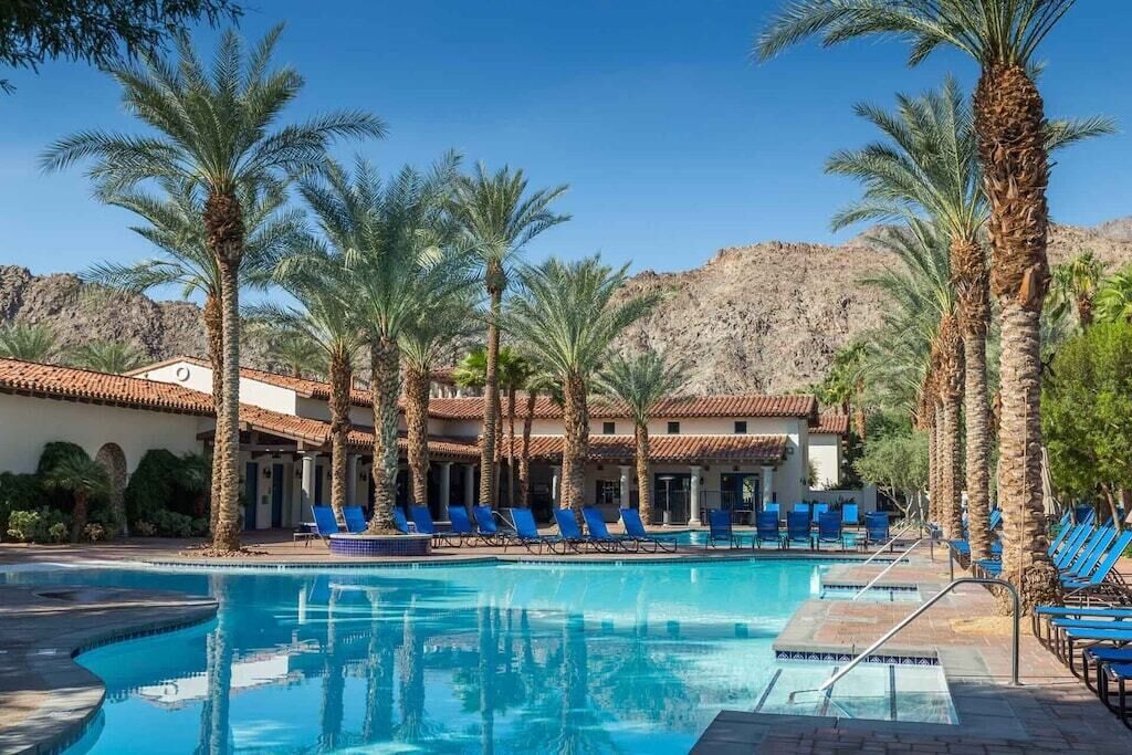 A pool area with palm trees and blue lounge chairs.