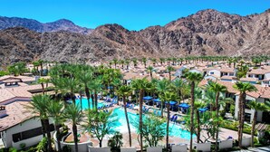 A resort with a central swimming pool surrounded by palm trees and lounge chairs, set against a backdrop of mountains. - Legacy Villas Near Main Pool Ground Floor Kitchen Resort#A (La Quinta)
