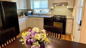 A modern kitchen with white cabinets, a black refrigerator, a stove, and a dining table with a floral centerpiece. - Sunnyvale Cabin (Sunnyvale)