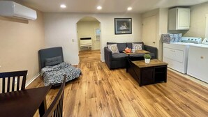 A living room with a sofa, a coffee table, and a dining table. There is a kitchen area with a stove and a washing machine. - Sunnyvale Cabin (Sunnyvale)