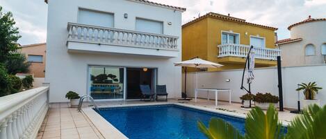A residential building with a swimming pool, a balcony, and a patio area with outdoor furniture.