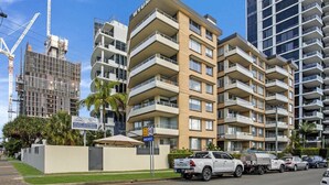 A multi-story residential building with balconies, a driveway, and parked vehicles. - Waterfront at Wyuna (Burleigh Heads)