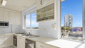 A modern kitchen with white cabinets, a dishwasher, a microwave, and a window with a view of a tall building. - Waterfront at Wyuna (Burleigh Heads)