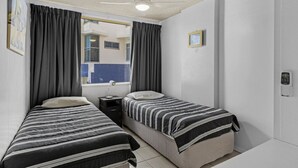 A room with two single beds, a desk, a chair, a ceiling fan, and a window with curtains. - Waterfront at Wyuna (Burleigh Heads)