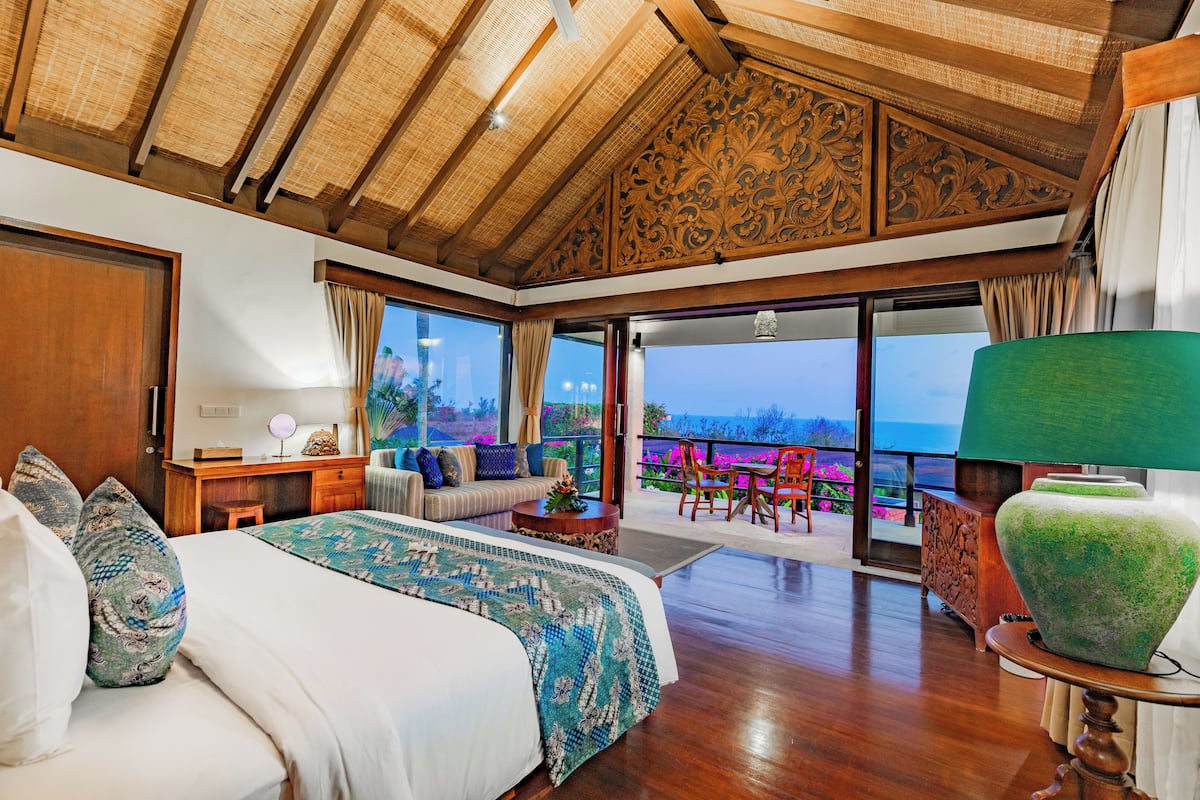 Ein geräumiges Schlafzimmer mit einem großen Bett, einer Sitzecke mit Sofa und Sesseln, einer Holzbalkendecke und einem Balkon mit Aussicht.